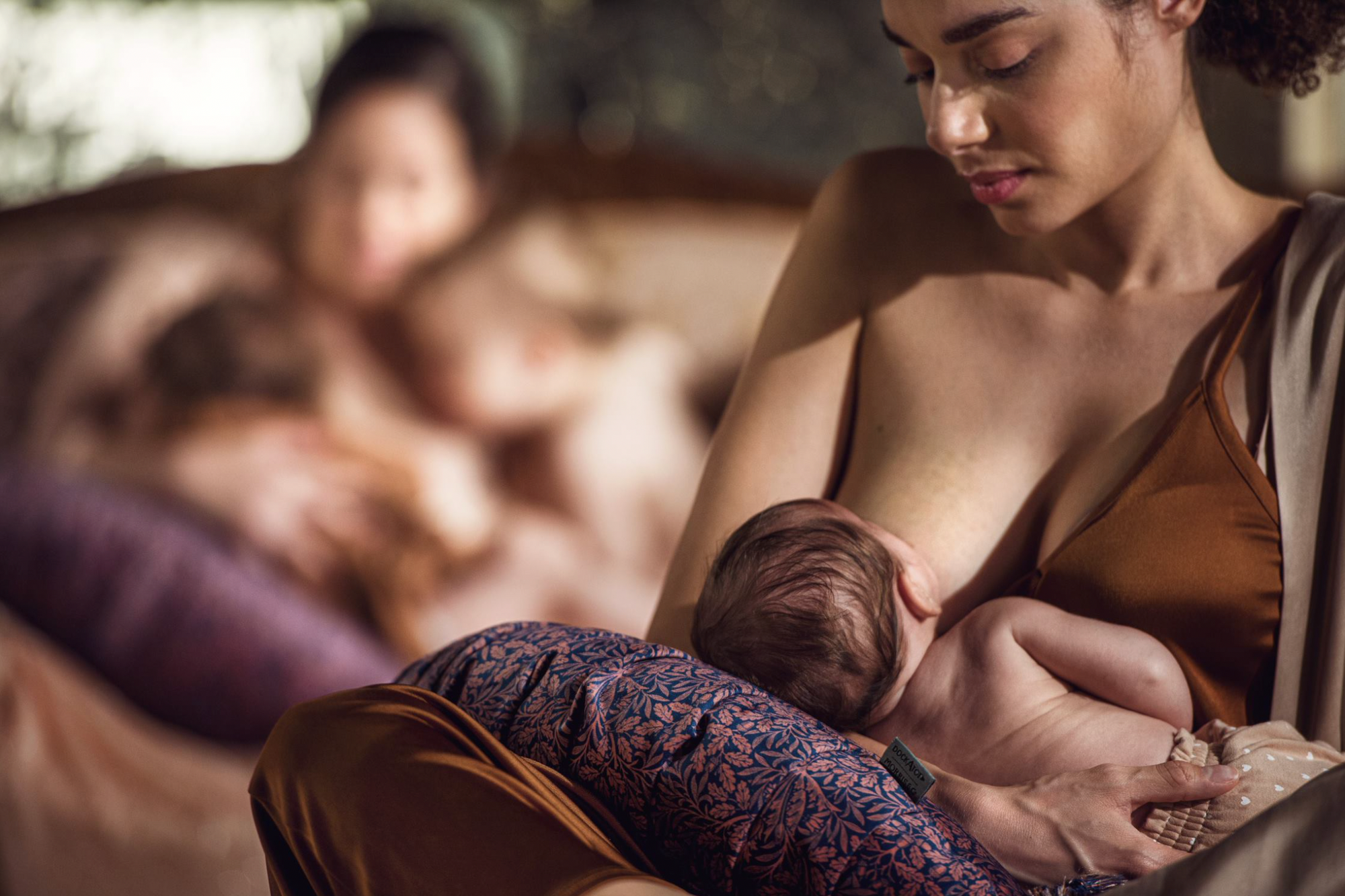 Mother breastfeeding baby with a DockATot nursing pillow in Acorn print